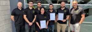 Passive Fire NZ team proudly holding ISO 9001, ISO 45001, and ISO 14001 certification certificates outside company office”