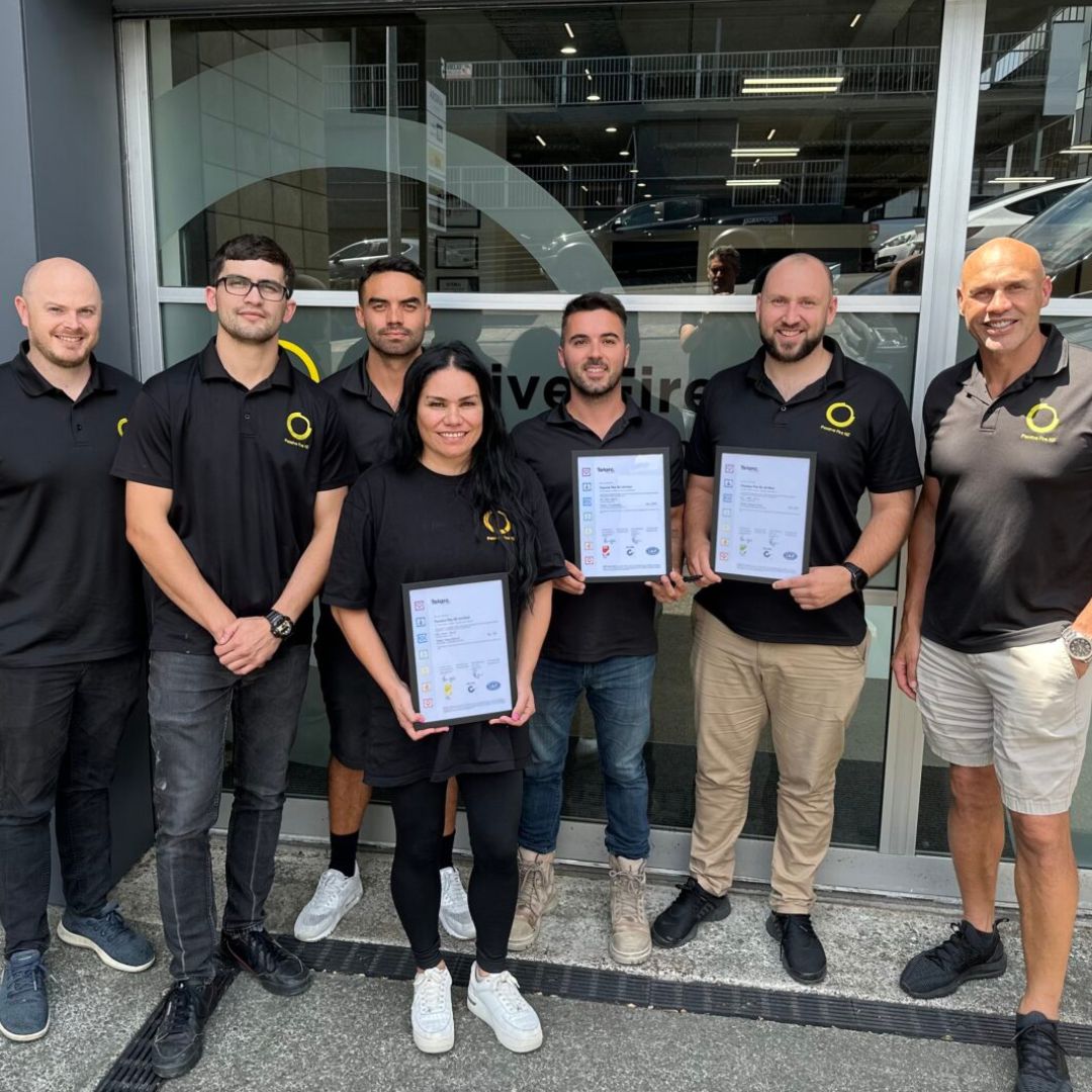 Passive Fire NZ team proudly holding ISO 9001, ISO 45001, and ISO 14001 certification certificates outside company office”