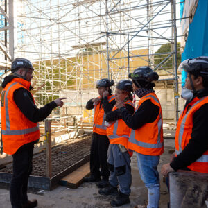 Passive Fire NZ team conducting a health and safety briefing on a construction site in high-vis gear and helmets.
