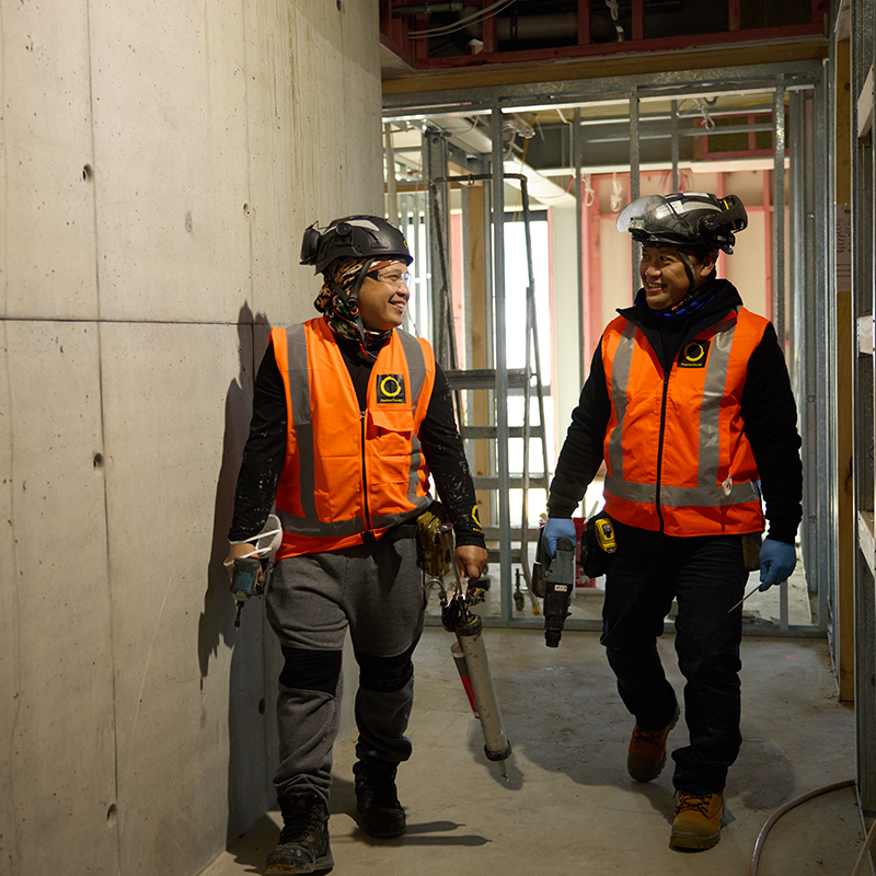 Two Passive Fire NZ installers walking through a construction site in safety gear, ready for installation.
